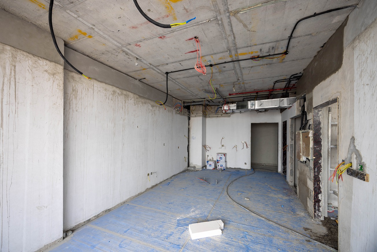 Beach Walk Residence An empty, unfinished room with bare walls, exposed wiring, and blue flooring, showing construction progress.